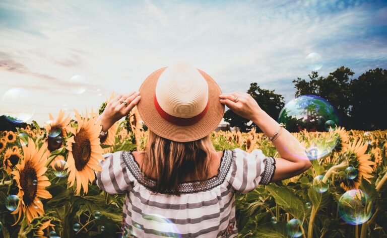Frau mit Sonnenhut steht im Sonnenblumenfeld