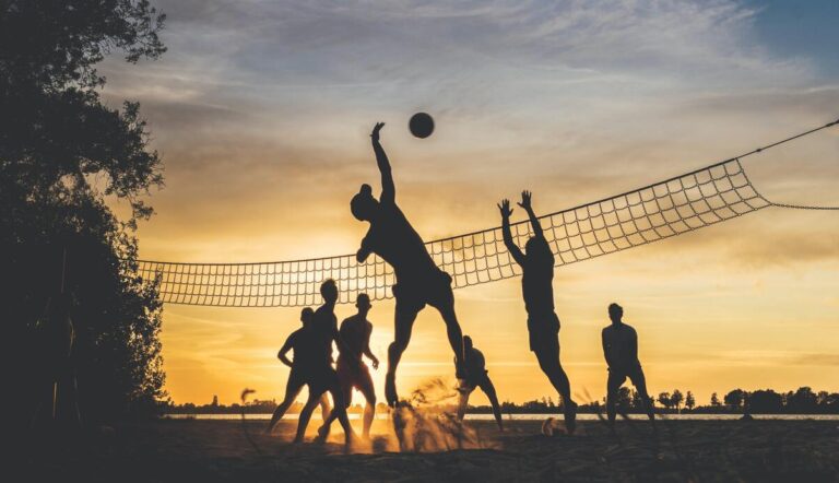 Mehrere Personen spielen Beachvolleyball im Sonnenuntergang