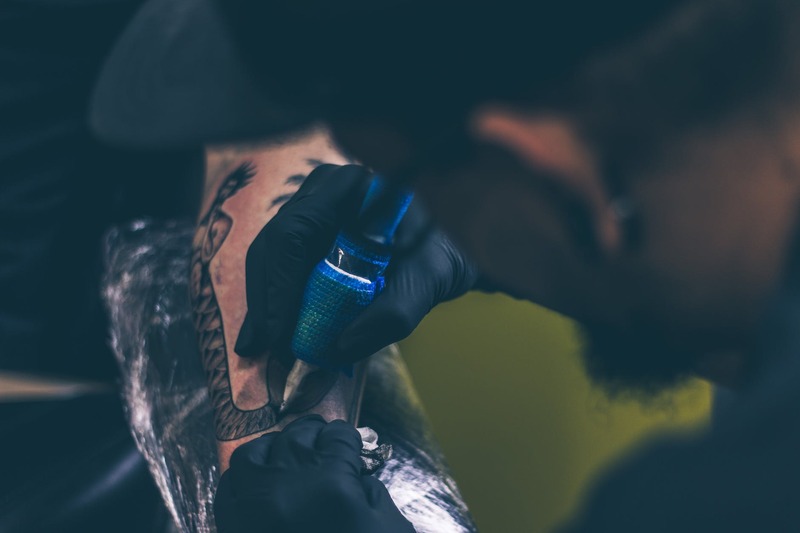 Symbolbild Tattooentfernung Milchsäure: Mann sticht Person Tattoo