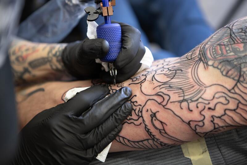 Symbolbild Tattoo entzündet welche Salbe: Mann wird am Oberarm tätowiert
