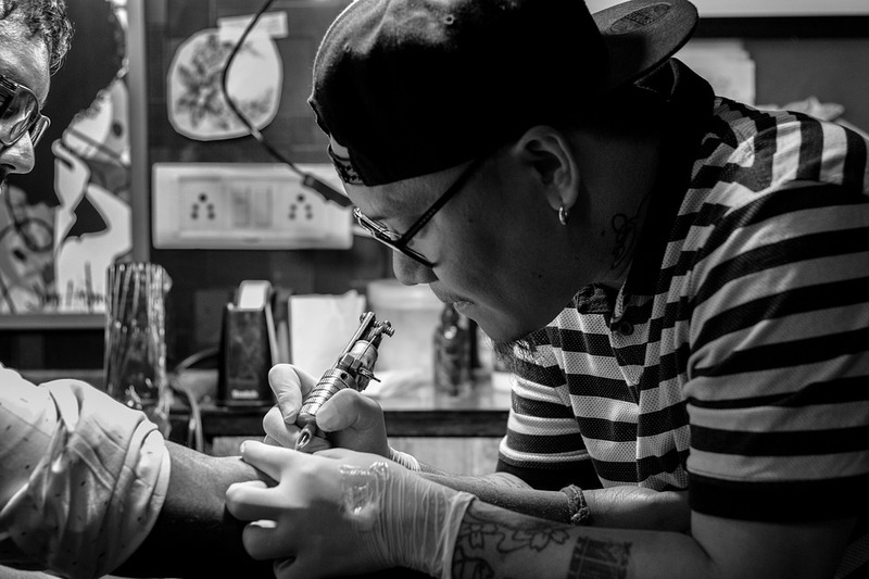 Symbolbild Krank durch Tattoo: Tätowierer sticht Tattoo auf Unterarm