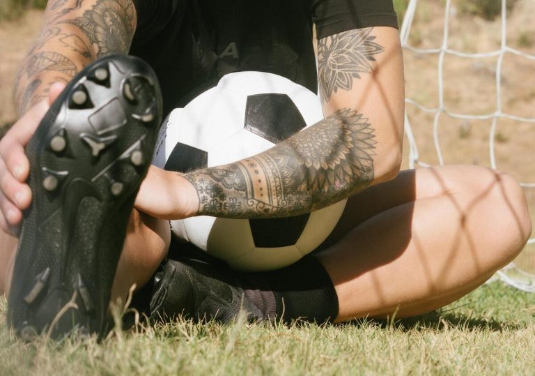 Tätowierter Fußballspieler mit Fußball in dem Arm